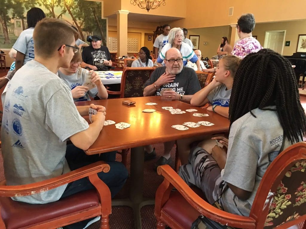 An intergenerational group of young adults and seniors engaged in a friendly card game at a community center, fostering social connection.